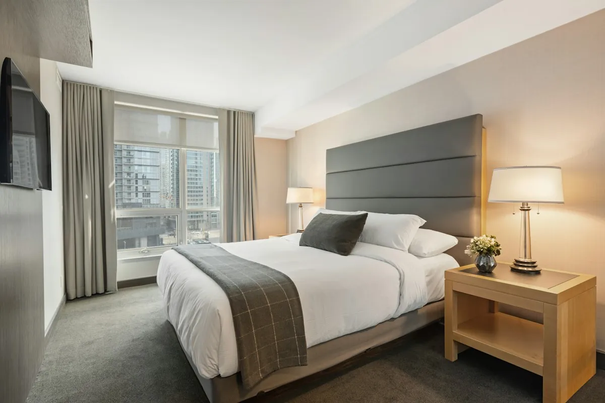 Cozy bedroom with layered linen bedding, warm bedside lamp and natural wood nightstand